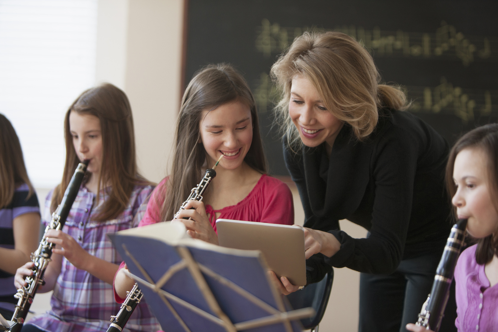 Caucasian teacher with digital tablet helping students in music class